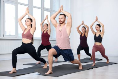 Sınıftaki minderler üzerinde yoga yapan bir grup insan.