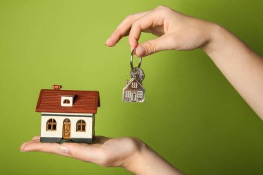 Yeşil arka planda ev modeli ve anahtarı olan kadın, yakın plan.