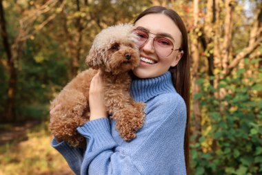 Sonbahar parkında sevimli köpeğiyle gülümseyen kadın.