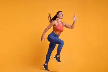 Spor giyimli kadın turuncu arka planda koşuyor.