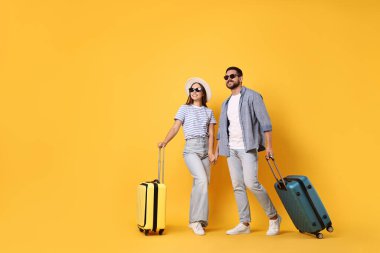 Turuncu arka planda bavulları olan güneş gözlüklü mutlu bir çift.