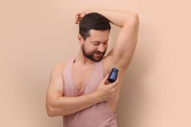 Adam bej arka planda roll-on deodorantı uyguluyor