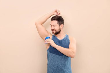 Gülümseyen adam bej arka plana katı deodorant sürüyor.