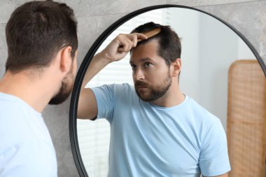 Adam aynanın içinde saçını tarıyor. Alopecia sorunu