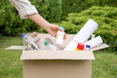 Geri dönüşüm konsepti. Dışarıdaki karton kutuya plastik şişe koyan kadın, yakın plan.
