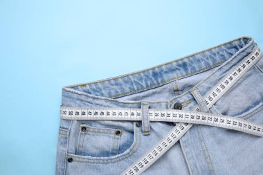 Açık mavi arka planda kot pantolon ve mezura, üst görünüm