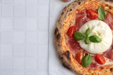 Delicious pizza with burrata cheese, basil, tomato and ham on white tiled table, top view. Space for text clipart