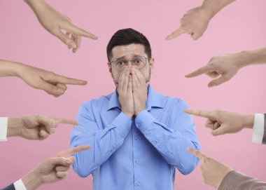 İnsanlar pembe arka planda mahcup bir adamı işaret ediyor.