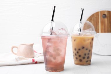 Tasty bubble tea in plastic cups on white tiled table clipart