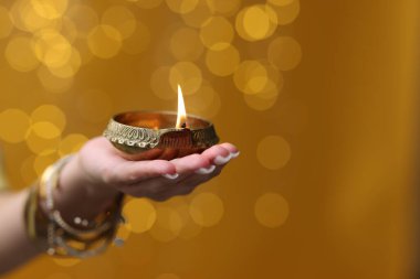 Diwali kutlaması. Elinde yanan diya lambası tutan bir kadın. Arka planda bulanık ışıklar var. Yakın plan. Metin için boşluk