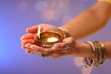 Diwali kutlaması. Renkli arka planda yanan diya lambasını tutan bulanık ışıklı kadın, yakın plan