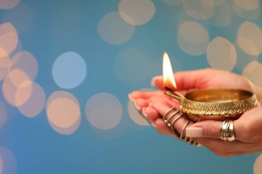 Diwali kutlaması. Açık mavi arka planda ışığı olan, bulanık ışıkları olan bir kadın, yakın plan. Metin için boşluk