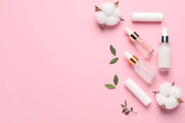 Farklı kozmetik ürünleri, pembe arka planda yapraklar ve pamuk çiçekleri, düz yatak. Metin için boşluk