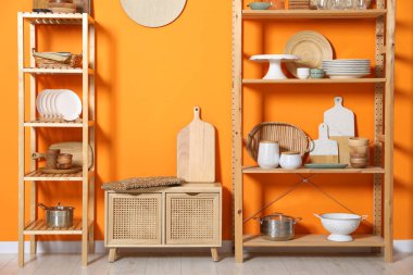 Ahşap depolama standı ve dolapta turuncu duvarın yanında mutfak malzemeleri var.