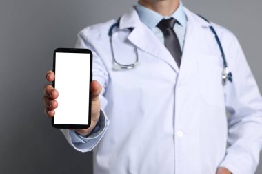 Doktor gri arka planda boş ekranlı akıllı telefonu gösteriyor, yakın plan. Tasarım için model