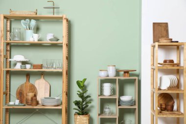 Ahşap depolama stantları ve mutfak gereçleri olan raf ünitesi yeşil duvarın yanında.