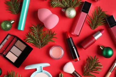 Kırmızı arka planda makyaj ürünleri ve Noel dekoru olan düz konum