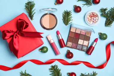 Açık mavi arka planda makyaj ürünleri ve Noel dekoruyla düz konum