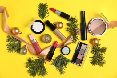 Sarı arka planda makyaj ürünleri ve Noel dekoru olan düz konum