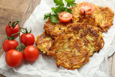 Lezzetli patates krepleri, domatesler ve maydanozlar ahşap masada, yakın plan.