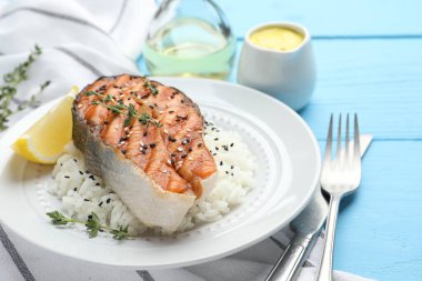 Lezzetli ızgara somon bifteği pilav, kekik, limon ve susam tohumları açık mavi ahşap masada, yakın plan.