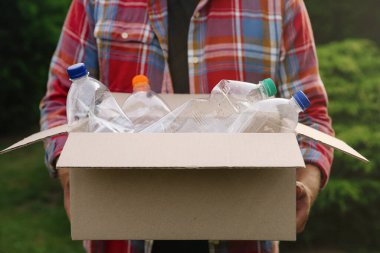 Geri dönüşüm. Elinde plastik şişelerle karton kutu tutan adam, yakın plan.