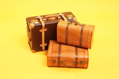 Sarı arka planda üç farklı kapalı bavul.