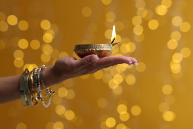 Diwali kutlaması. Renkli arka planda yanan diya lambasını tutan bulanık ışıklı kadın, yakın plan