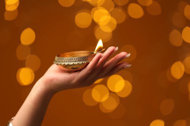 Diwali kutlaması. Kahverengi arka planda yanan diya lambası tutan kadın, yakın plan.