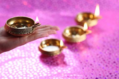 Diwali kutlaması. Pembe arka planda yanan diya lambasını tutan kadın, yakın plan.