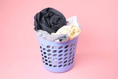 Pembe arka planda içi çamaşır dolu plastik sepet.