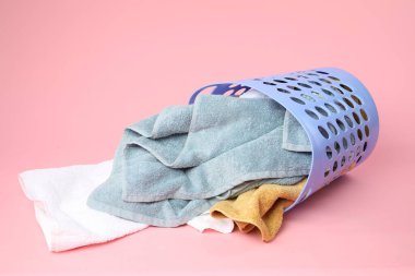 Pembe arka planda içi havlu dolu çamaşır sepeti devrilmiş.