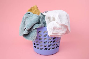 Pembe arka planda içi çamaşır dolu plastik sepet.