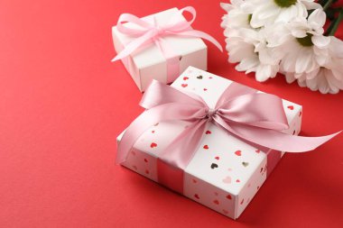 Kırmızı arka planda fiyonklu hediye kutuları ve çiçekler