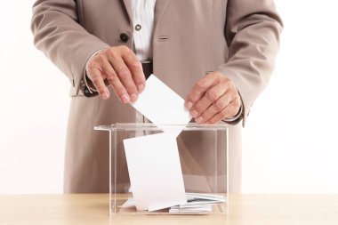 Referandum. Tahta masada, beyaz arka plana karşı oy sandığına koyan adam, yakın plan.