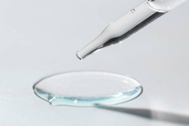 Işık arkaplanındaki pipetten akan kozmetik serumu, yakın plan