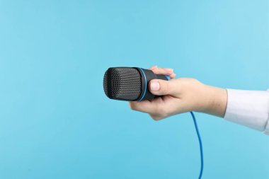 Açık mavi arka planda mikrofonu olan kadın, yakın plan.