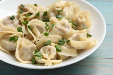 Mavi ahşap masada yeşil soğanlı leziz pelmeni, yakın plan.