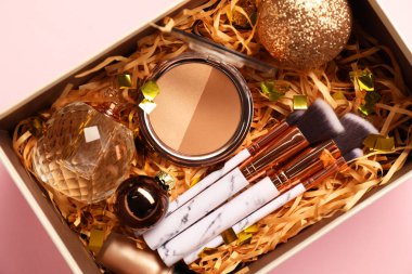 Makyaj fırçaları, dekoratif kozmetik, parfüm ve Noel dekoru pembe arka planda, üst görünümde.