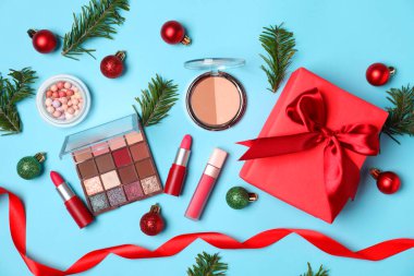 Açık mavi arka planda makyaj ürünleri ve Noel dekoruyla düz konum