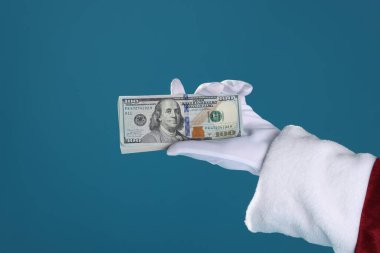 Mavi arka planda dolar banknotları tutan Noel Baba, yakın plan. Metin için boşluk