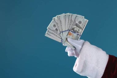 Mavi arka planda dolar banknotları tutan Noel Baba, yakın plan. Metin için boşluk