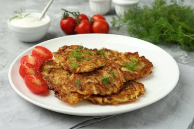 Gri masada servis edilen taze domatesli leziz patates krepleri, yakın plan.