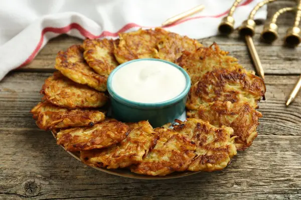Lezzetli patates krepleri, ekşi krema, menorah ve ahşap masa üzerindeki mumlar, yakın plan. Hanuka bayramı yemekleri.