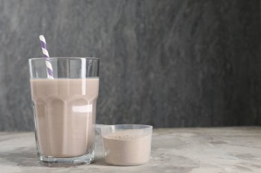 Lezzetli protein karışımı bardakta ve toz tozu ile gri masada, metin için boşluk