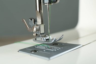 Gri arkaplanda yeşil iplikli dikiş makinesi, yakın plan
