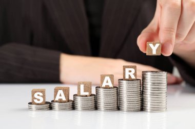 Kadın sözel maaşlı tahta küpleri ve para yığınlarını beyaz masaya koyuyor, yakın plan.