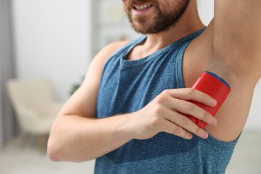 Gülümseyen adam evde deodorant sürüyor, yakın plan.