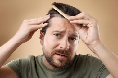 Adam saçlarını bej arka planda tarıyor. Alopecia sorunu
