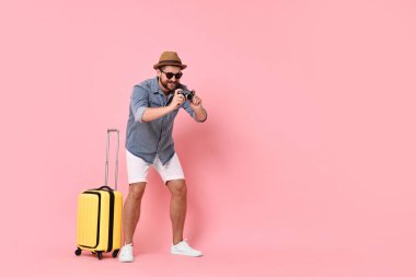 Klasik fotoğraf makinesi ve pembe arka planda bavulu olan mutlu adam, mesaj için yer var.